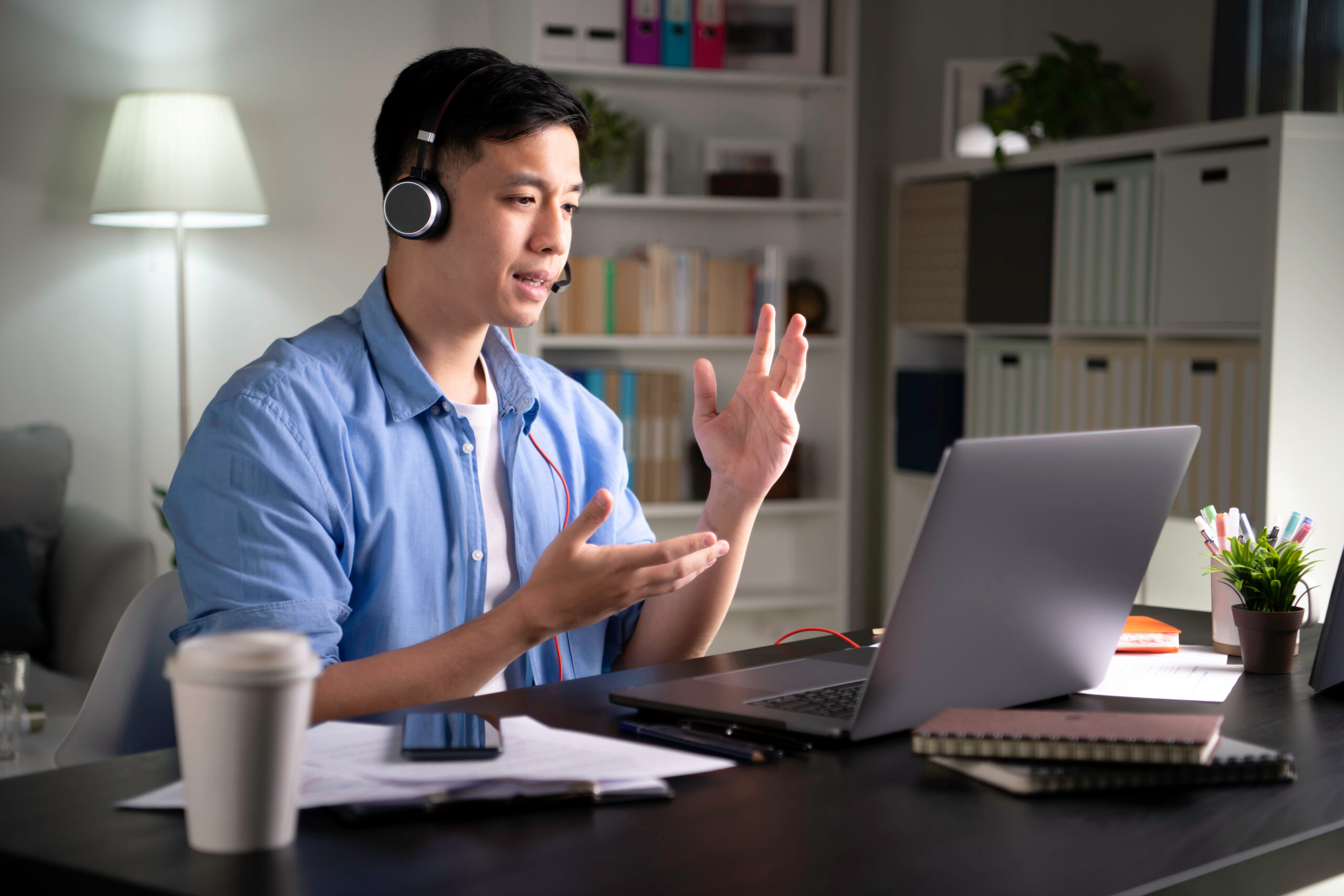Focused young Asian business person, entrepreneur, speaker, student, office worker wearing headphones, looking at laptop screen and speaking in video conference call, giving lecture, joining online class using a laptop when work from home.